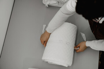 a female employee of a clothing workshop ties a roll of prepared white fabric; fabric preparation before sending for other production processes