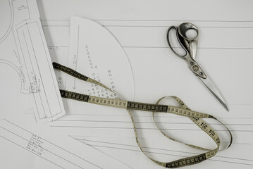 paper with a drawing on which scissors and a flexible ruler lie; tools for cutting and sewing a...