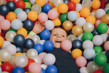 child having fun in colorful dry pit. Smiling happy boy in playroom