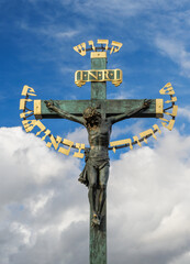 Christian Crucifixion, bronze statue of Jesus Christ, decoration on the Charles Bridge in Prague. The Catholic Crucifix with religion message at cloudy sky background.