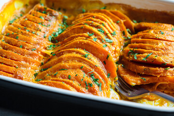 Roasted sweet potato gratin with parsley in ceramic pan. Vegan healthy recipe concept.