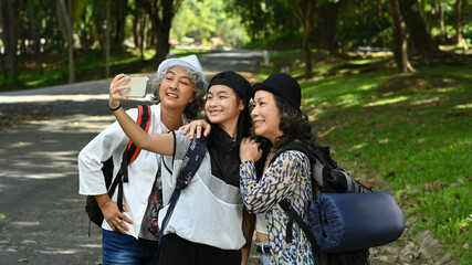 Joyful asian girl with holding smartphone and taking selfie with lovely elderly women while walking in the park