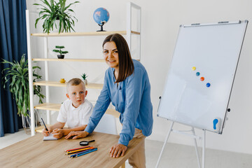 Attentive young woman tutor teacher helping little boy pupil with studying, correct mistakes explain learning material. Smiling mother assist small boy with home task