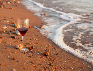 A glass of red wine stands on the shore of the Adriatic Sea at sunset