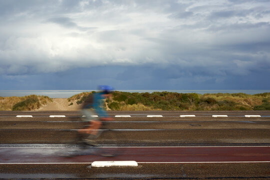 1 male cyclist in Holland in motion. Young man cycling on his road bike in rainy weather. Netherlands, Zeeland, Brouwersdam.
