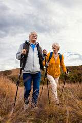 Active senior couple with backpacks hiking together in nature on autumn day.