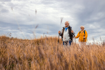 Active senior couple with backpacks hiking together in nature on autumn day.