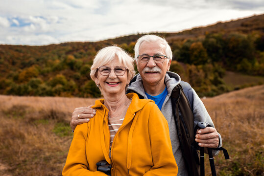 Portrait of active senior couple with backpacks hiking together in nature on autumn day.