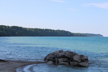 Stack of rocks on the lakeshore with clear blue water and green forests in the background