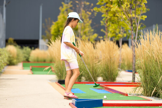 Cute Preschool Girl Playing Mini Golf With Family. Happy Child Having Fun With Outdoor Activity. Summer Sport For Children And Adults, Outdoors. Family Vacations Or Resort.