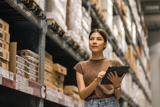 Young female manager worker checklist manage parcel box product in warehouse. Asian woman supervisor using tablet working at store industry. Logistic import export concept.