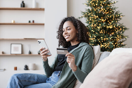 Young woman ordering gift during Christmas holiday at home using smartphone and credit card. Shopping online during holidays, internet banking, store online, spending money, winter holiday concept.
