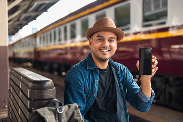 Traveler young asian man using cellphone booking trip at terminal train station. Happy tourist...
