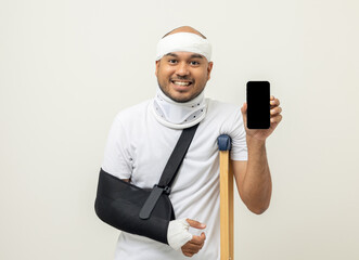 Happy young asian man broken arm holding smartphone. Asian man put on plaster bandage cast splint. Male patient wearing sling support arm after accident injury. life insurance and accident