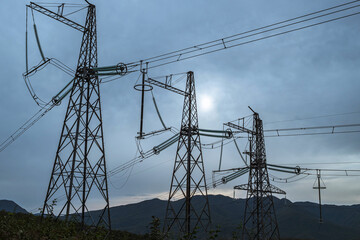 Transmission poles against the background of mountain hills and overcast sky. A concept of the global energy crisis. Electricity problems in Europe and in the world.