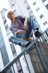 A teenage boy is sitting and posing in urban exterior surrounded by the buildings.