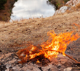 Bonfire burning against the background of dry grass and river in autumn Landscape