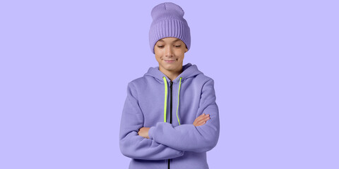 A teenager in a lilac sports jacket and a lilac knitted hat, stands smiling and looking down, on a...