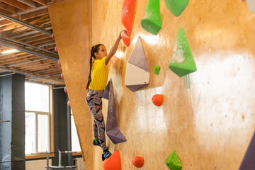 Junior Climber Girl shirt hanging on holds on climbing wall of indoor gym