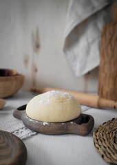 Fototapeta na wymiar Yeast dough on a plate. Home atmosphere. Nearby lies a rolling pin and wooden bowls. Side view.