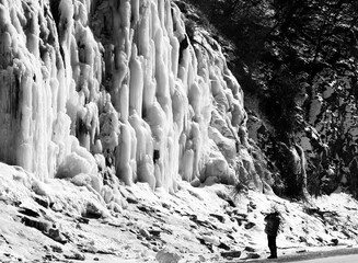 Fototapeta na wymiar Man makes photo of icy mountain waterfall. Winter in Georgia. Black and white.