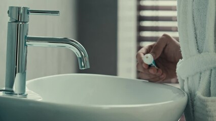 Close-up side view male hands in bathrobe holding bamboo wooden dental toothbrush squeezing out tube of whitening toothpaste preparation for brushing teeth toothy oral dental hygiene anti caries care