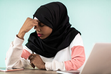 afro girl wearing a hijab is disappointed and sad sitting in her home office and using a laptop