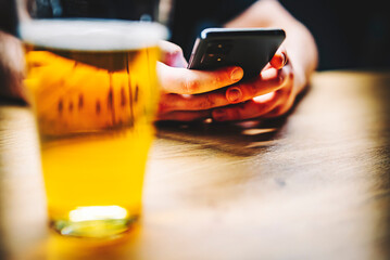 close up of man hand hold smartphone, drinking beer and reading message at bar or pub
