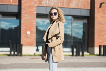 Fototapeta premium Portrait of a young Caucasian girl in a coat and sunglasses in the city on an autumn day.
