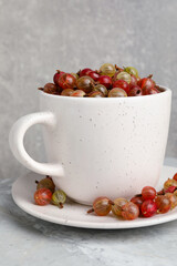 Cup with ripe gooseberries on light grey marble table
