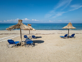 A deserted beach with sun bed and natural umbrella with a view of the horizon and deep blue sea.