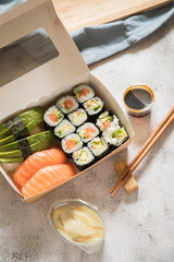 Lachs Avocado Erdnuss Maki und Nigiri Sushi vom Lieferdienst mit Ingwer, Sojasoße und Holz Stäbchen in Verpackung auf Stein Hintergrund hell
