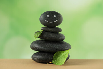 Stack of stones with drawn happy face and green leaves on table against blurred background. Zen concept