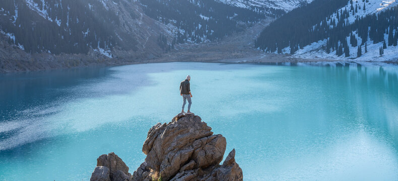 One Man Standing On A Boulder On A Vantage Point Over Mountain Lake