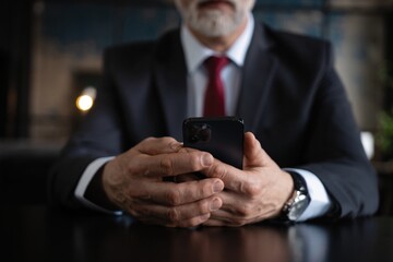 Close-up of businessman hands holding smartphone while sitting at desk.