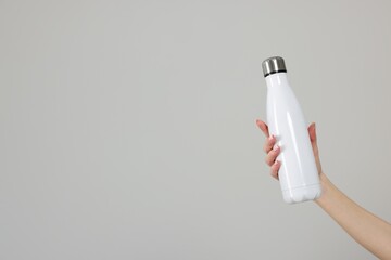 Woman holding thermos bottle on light grey background, closeup. Space for text