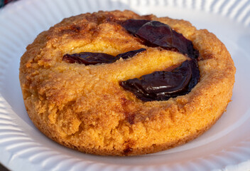 Close-up of a plum polenta cake served on a white paper plate.