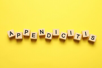 Word Appendicitis made of wooden cubes with letters on yellow background, top view