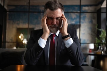 Frustrated mature man sitting in a modern office. Overworked businessman with terrible migraine