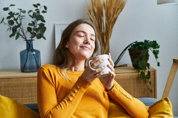 Relaxed woman smelling coffee in the morning sitting in the living room at home.