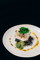 Baked fish on a rice pillow with cuttlefish ink, garnished with seaweed and papaya sauce.