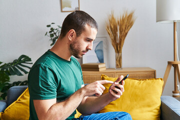 Serious man using cell phone sitting on a sofa in a house