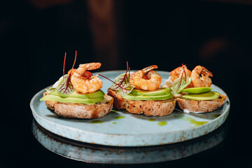 Bruschetta with avocado and shrimp, on crispy dried bread, decorated with greens.