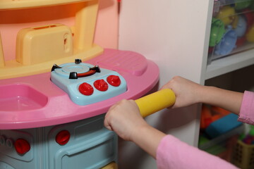 Сhild's hand is playing with a toy rolling pin on kitchen stove in the childrenroom