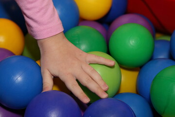 Child's hand on colorful plastic balls : blue, yellow, green, purple . Children play room leisure
