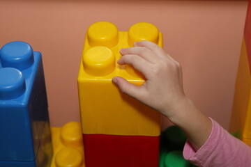Child's hand puts a large colorful construction blocks from the children's model kit in the creche...