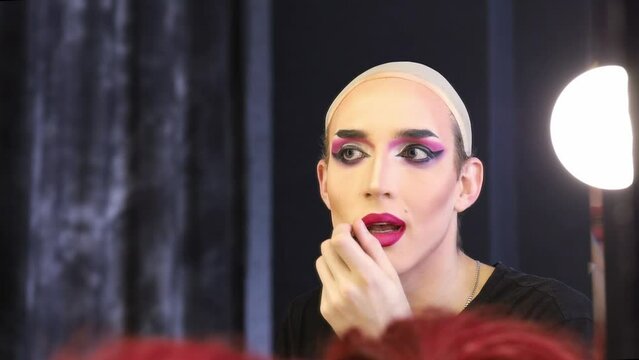 Young performer wearing hairnet applying lipstick in front of mirror