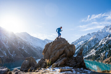 Man climbing on a huge boulder on a vantage point over a mountain lake