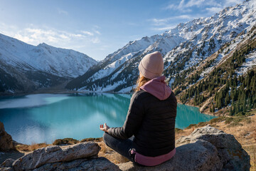 Back view of a woman meditating on a vantage point over turquoise mountain lake