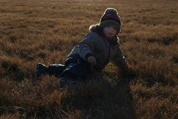 Little boy lies on his side on the brown autumn grass and looks at the camera